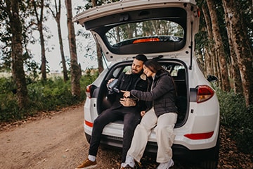two people happily sitting in the trunk of their car, watching videos on their cam recorder