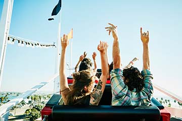 ear view of couple with arms raised on roller coaster in amusement park