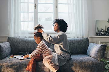 A woman does her daughter's hair while sitting on the couch