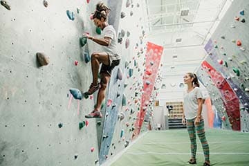 Beginner learns to rock climb on a bouldering wall with encouragement from a friend