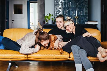 Single mom sitting on sofa with daughters and family dog.
