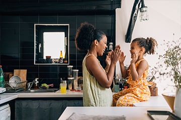 A mother and daughter smile while playing a game together in the kitchen of their home.
