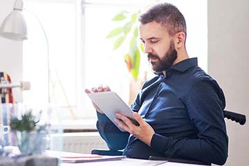 Businessman in wheelchair with tablet in his office