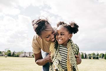 Mom hugging daughter from behind while playing outside