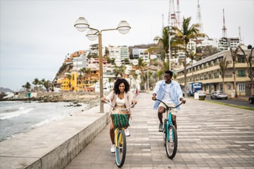 Young couple riding bikes down a beach boardwalk while on vacation.