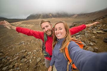A couple takes a selfie in front of a volcano.