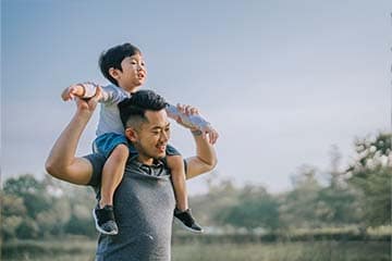 Young man smiles while a child sits on his shoulders as they walk outside