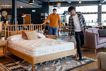 Two men examine a bed for sale inside a furniture store.