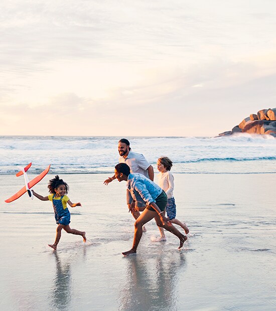Family of four runs on the beach, playing with a toy airplane