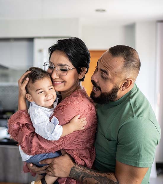 A happy family of three embrace in a modern kitchen.