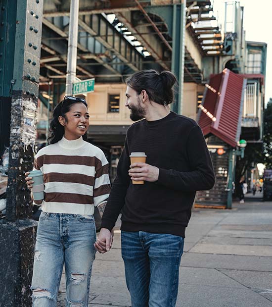 Couple walking down city street together with coffees in hand.