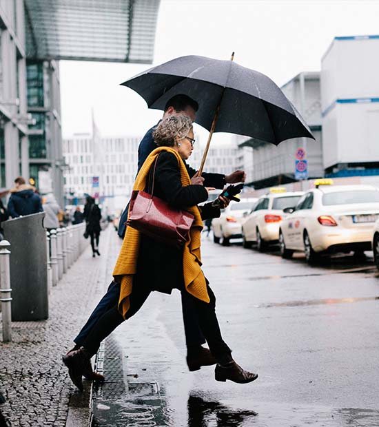 A couple crosses the street in the rain, sharing one umbrella