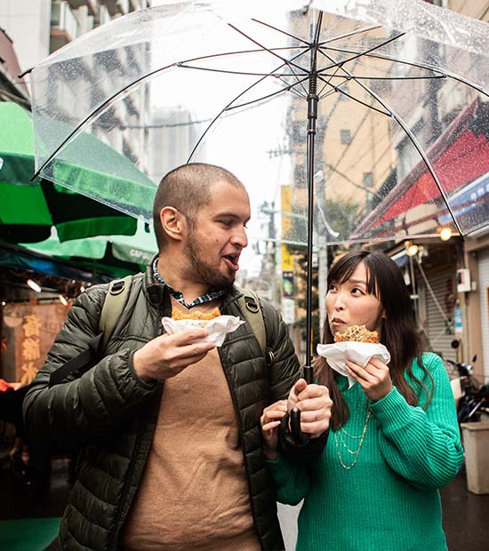 A married couple walks through a city street sightseeing while eating