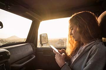 A woman is sitting in the passenger seat of a vehicle and looking at her phone.