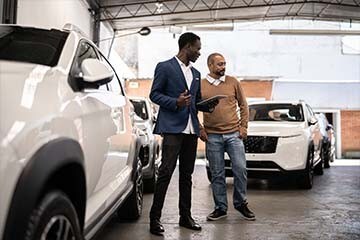 A car dealer and a customer looking at different cars at the dealership