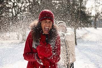 A woman gets hit in the back by a snowball during a snowball fight.