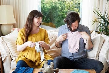 Couple sitting on couch in living room looking at baby clothes.