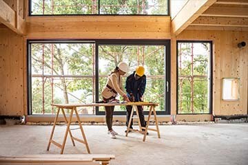 A man and woman stand inside a new construction and look at a blueprint for the home.