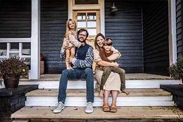 A family poses for a portrait on the front porch steps of a farmhouse.