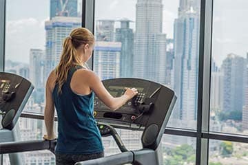 Woman exercising on treadmill in gym against the background of a big city.