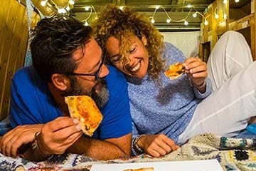 Man and woman laying down laughing and eating pizza.