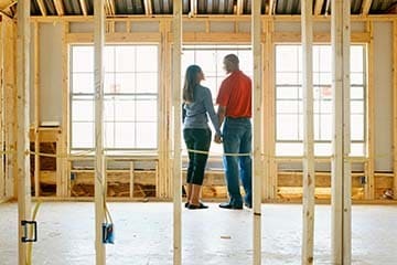 A couple is holding hands and looking at each other while standing in their home under construction.