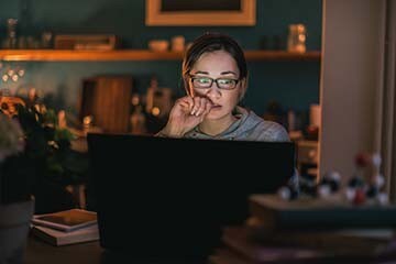 Woman biting nail looking at laptop at home