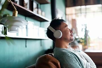 Young man with eyes closed, enjoying music on his headphones while relaxing on a sofa.