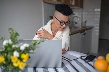 Woman in eyeglasses drinks her morning coffee while on her laptop