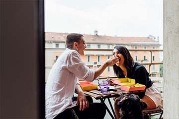Image of a couple feeding each other sushi on a balcony