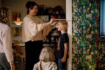  Mother measuring height of smiling son with book on door frame