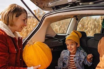 A mother and her two children are loading pumpkins into the trunk of her vehicle.