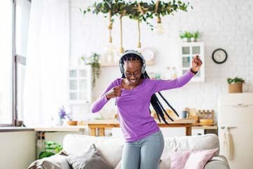 A happy woman has headphones on and is dancing in her living room.