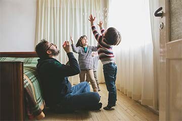 Image of a man blowing bubbles in bedroom with his three kids. 
