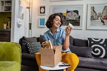 Woman sitting on her couch opening a box and unwrapping a vase she ordered online.