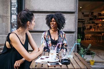 Two friends sitting and talking at a bistro table outside a restaurant.