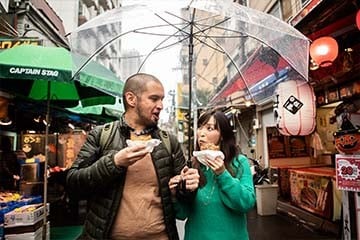 A married couple walks through a city street sightseeing while eating